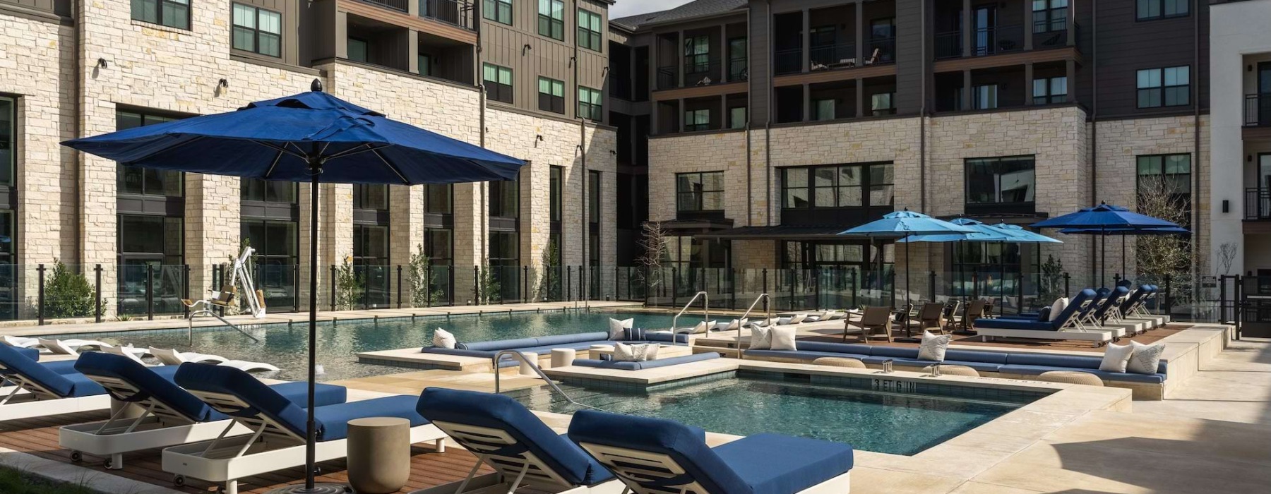 A courtyard pool with lounge chairs and umbrellas at The Mia North Austin apartments for rent.